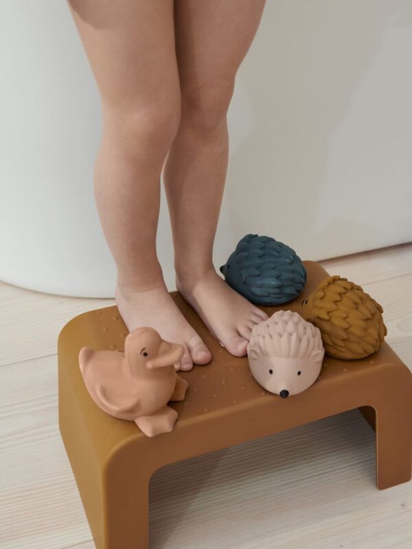 petite fille debout sur un tabouret avec des jouets pour le bain